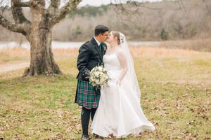 Elegant bride and groom share a romantic moment in their Scottish wedding attire in a rustic outdoor setting.