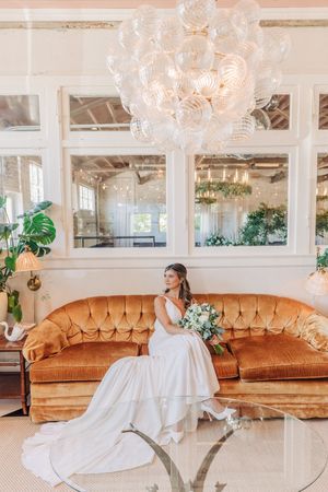 A glowing, elegant event space with crystal chandeliers, vintage velvet sofas, and flowing white bridal gown details.