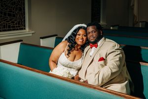 A couple in wedding attire sits together in a teal church pew during their celebration.