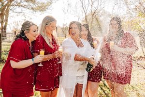 Group of friends in red and white outfits laughing together while spraying champagne outdoors in autumn setting.