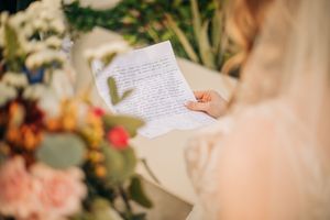 Someone writes on paper surrounded by soft pink and peach colored flowers and foliage in romantic lighting.