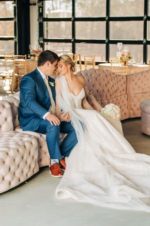 Newlyweds share an intimate moment while sitting on an elegant tufted beige sofa in an industrial-chic venue.