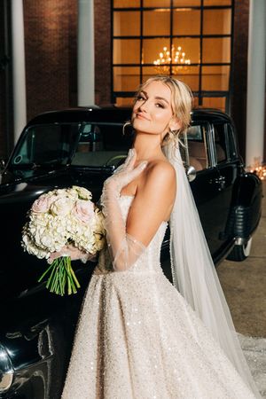A bride in a sparkly white wedding gown poses with an elegant bouquet of white roses and flowers.
