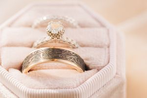 Wedding and engagement rings with intricate details rest in a light pink velvet ring box.