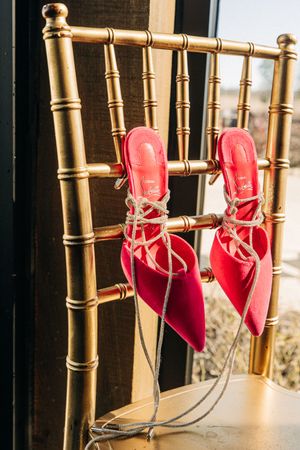 A pair of bright red ballet shoes with satin ribbons are tied to a gold bamboo chair back in natural light.