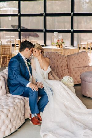 Newlywed couple shares intimate moment while seated on blush tufted sofa in elegant wedding venue.