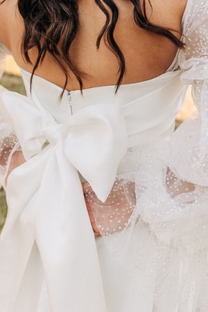 Close-up detail of a white bow and delicate polka dot tulle on the back of an elegant wedding dress.