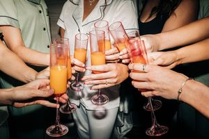 Multiple hands raising colorful cocktail glasses and champagne flutes in a celebratory toast during an event.