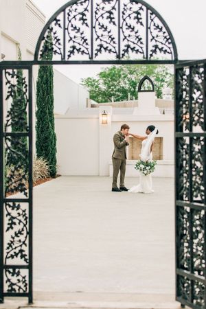 Wedding couple being photographed through an ornate arched iron gate with vine details during their elegant outdoor ceremony.