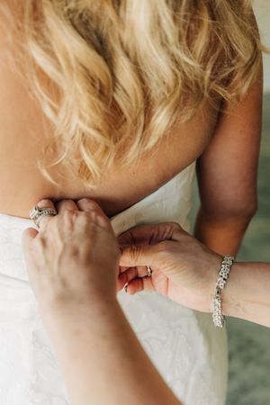 A close-up of hands adjusting a white wedding dress with sparkly jewelry and blonde wavy hair visible.