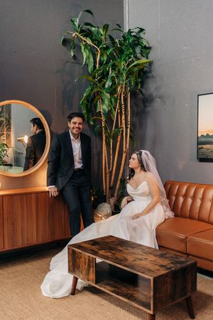 A couple shares intimate moments in a modern lounge setting with tan leather couch and decorative palm plants.