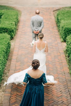 A couple and flower girl walk on a brick path lined with green hedges, shown from different angles.