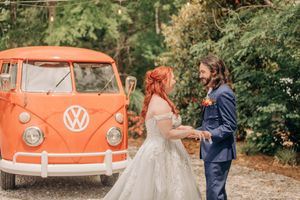 A vintage orange Volkswagen bus parked in an autumn forest setting creates a romantic backdrop for a photo session.