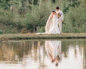A romantic lakeside wedding photoshoot captures a couple standing in shallow water with their reflections in the surface.