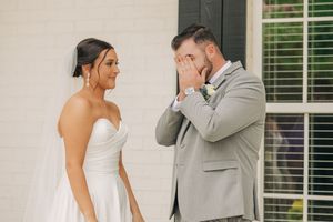 Groom in gray suit becomes emotional during first look with bride in white strapless wedding dress.