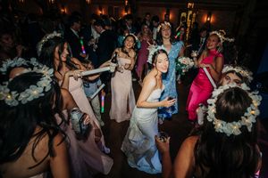 Wedding party dancing on a dark dance floor with floral headpieces and colorful dresses during reception celebration.
