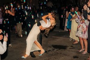 A couple shares a romantic dip dance move during their wedding reception while guests watch with sparklers at night.