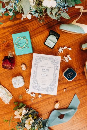 Wedding invitation cards and floral decorations arranged on a wooden surface with teal blue accents and white blossoms.