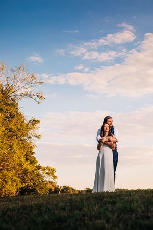 A couple enjoying a romantic sunset moment together in a golden meadow beneath a vibrant blue sky.