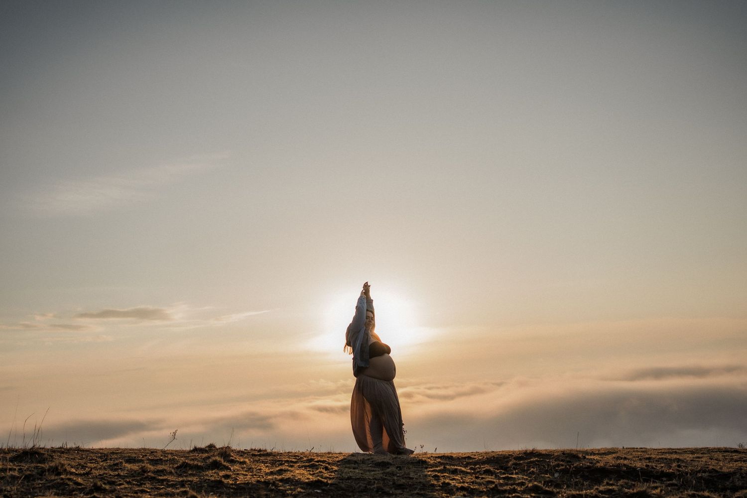 Silhouetted figure stands on rocky terrain with arms raised against a glowing sunset sky in Mansfield