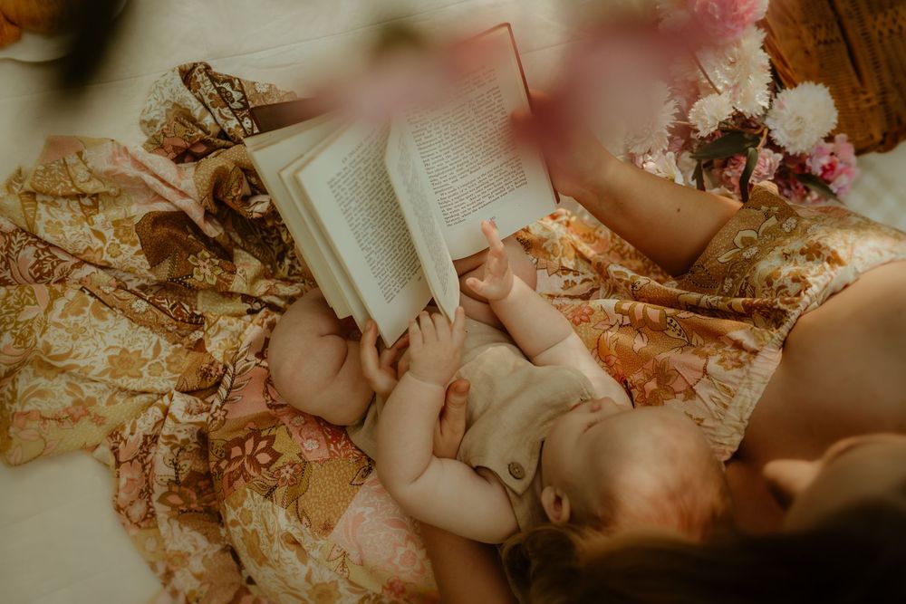 A book rests on ornate fabric with dried flowers creating a cozy reading scene in warm lighting.