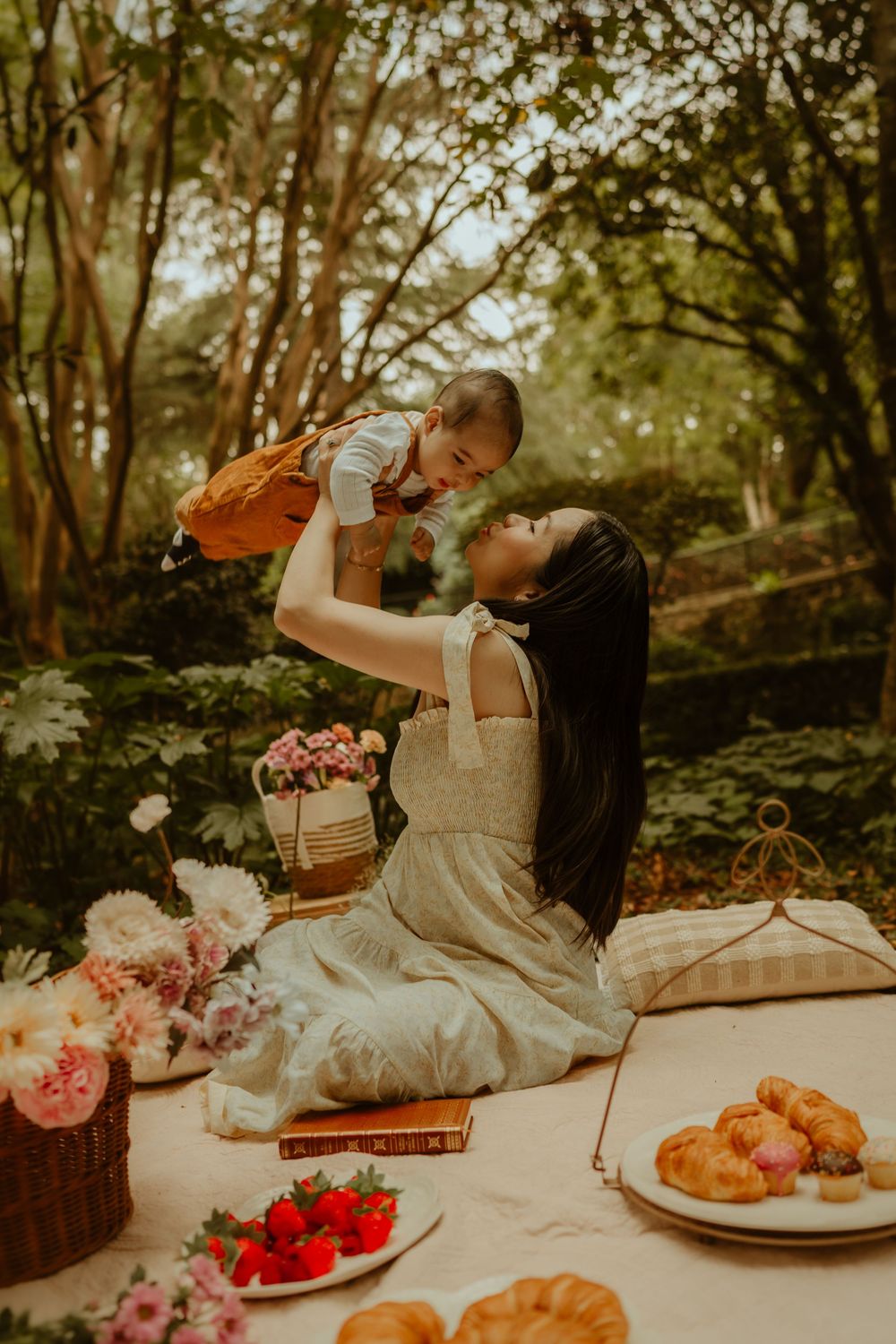 A rustic garden picnic scene with baked pastries, fresh strawberries and pink roses arranged on a blanket outdoors.