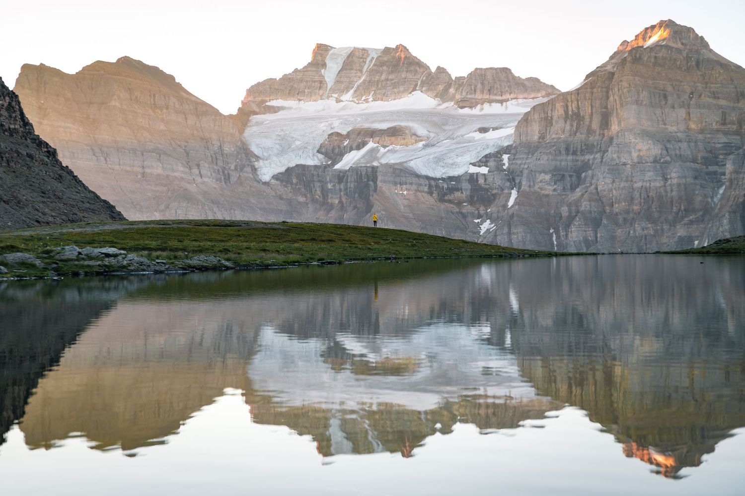 Calm mountain lake reflecting snow-capped peaks and rocky cliffs during sunset in the wilderness.