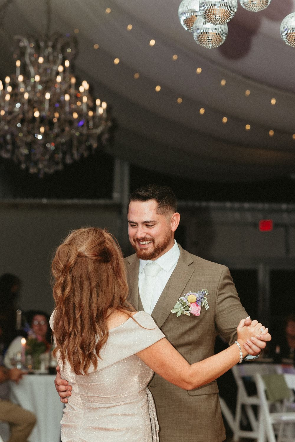 A couple shares an intimate dance moment under sparkling disco balls and chandeliers at an elegant reception venue.