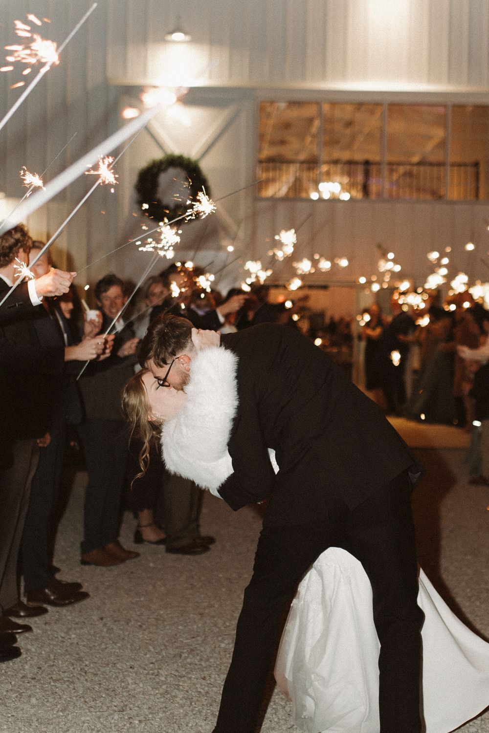 A romantic moment captured during a sparkler exit at a wedding reception with guests creating a magical tunnel of light.