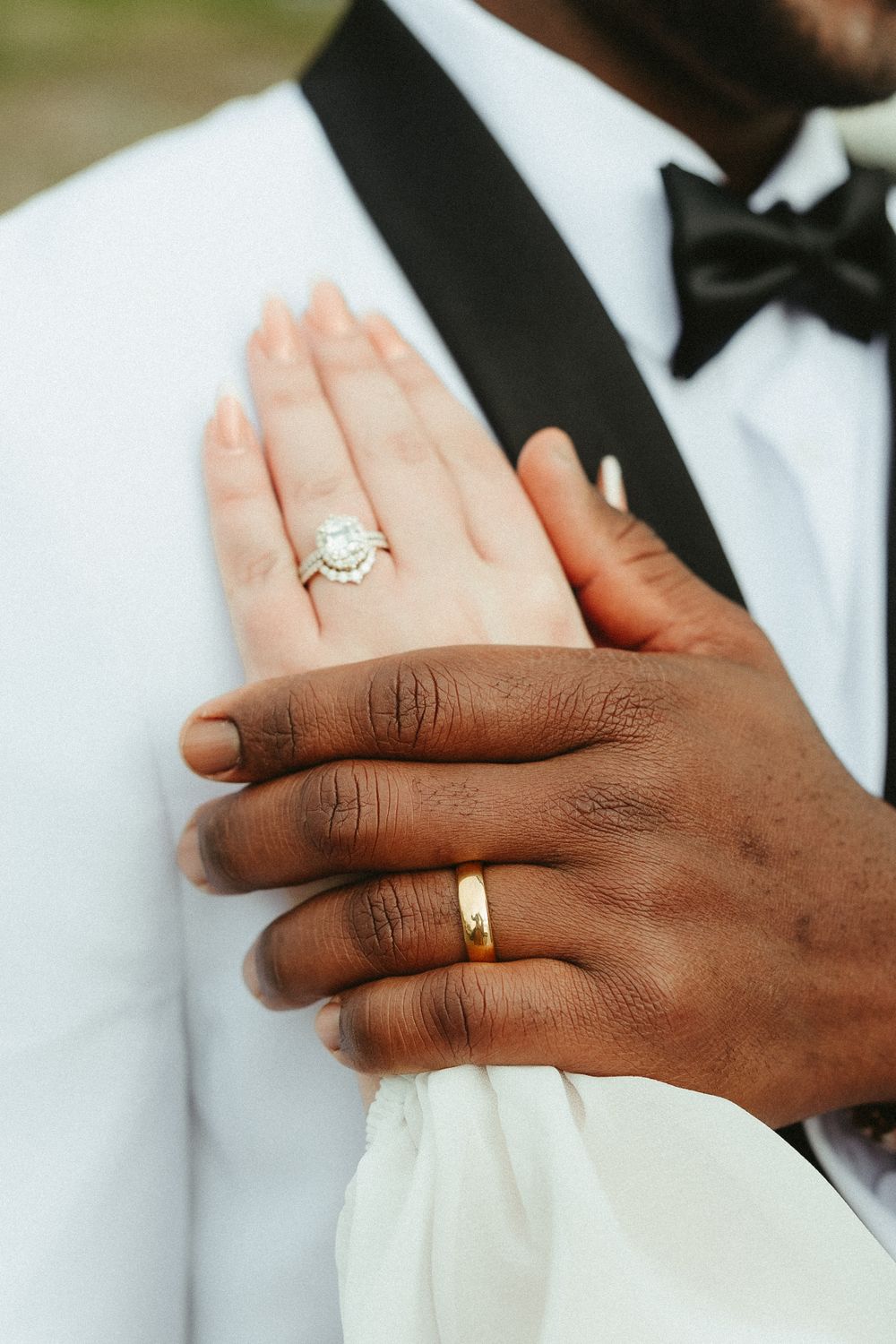 Close-up of newlywed couple's hands showing diamond engagement ring and gold wedding band against formal attire.