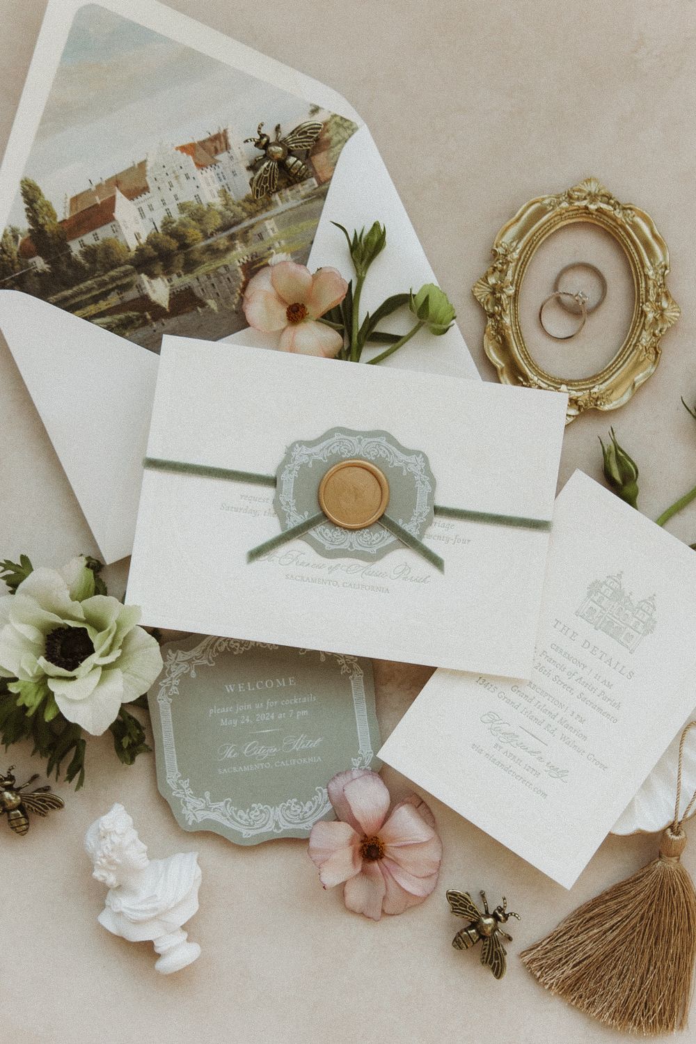 Elegant wedding invitation suite with white envelopes, gold wax seal, floral details and vintage frame holding wedding rings.