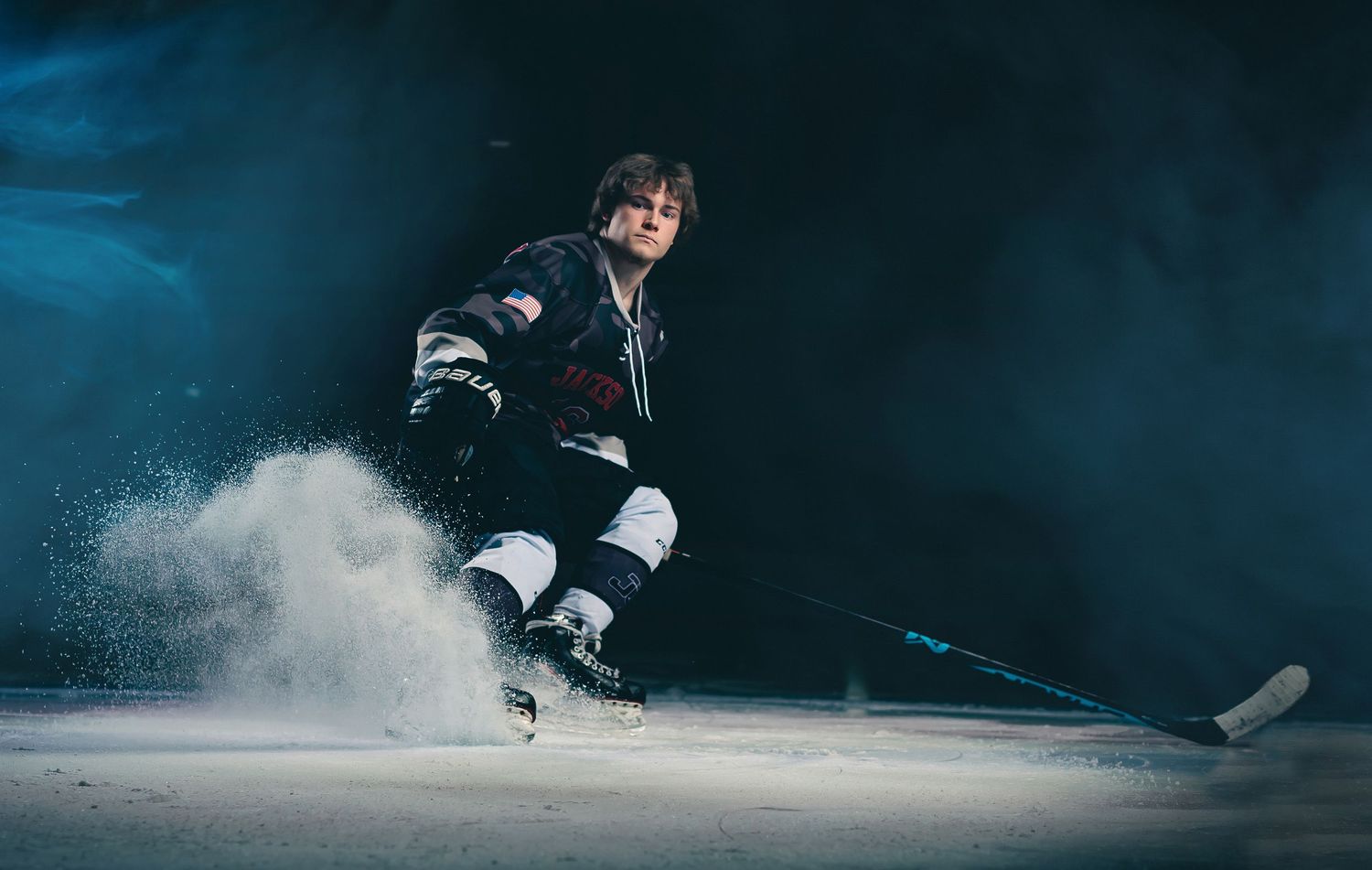 Hockey player spraying ice during dramatic action shot against dark background.