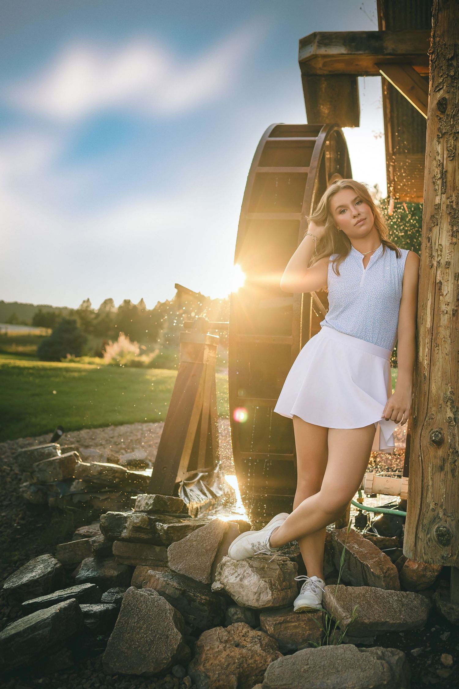 Summer portrait in white tennis dress against rustic water wheel at sunset.