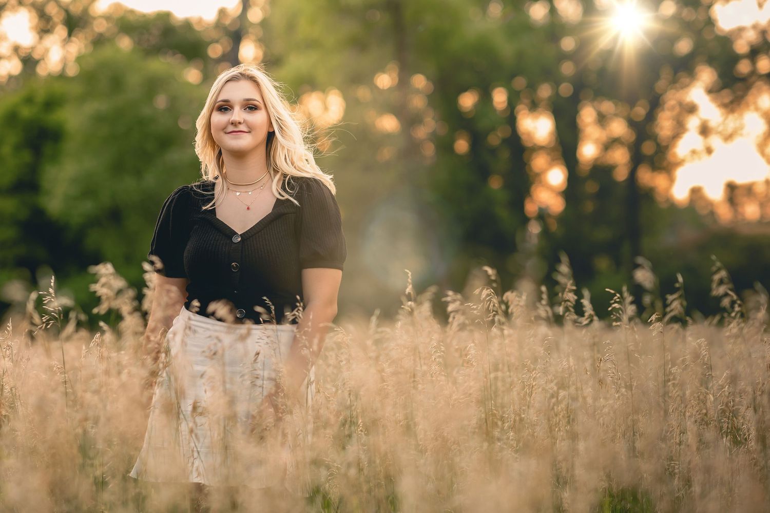 A golden sunset streams through tall grass in a serene outdoor portrait setting.