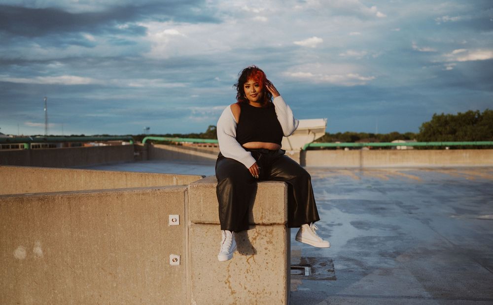Two people sit casually on a concrete wall overlooking a scenic beach landscape during golden hour.