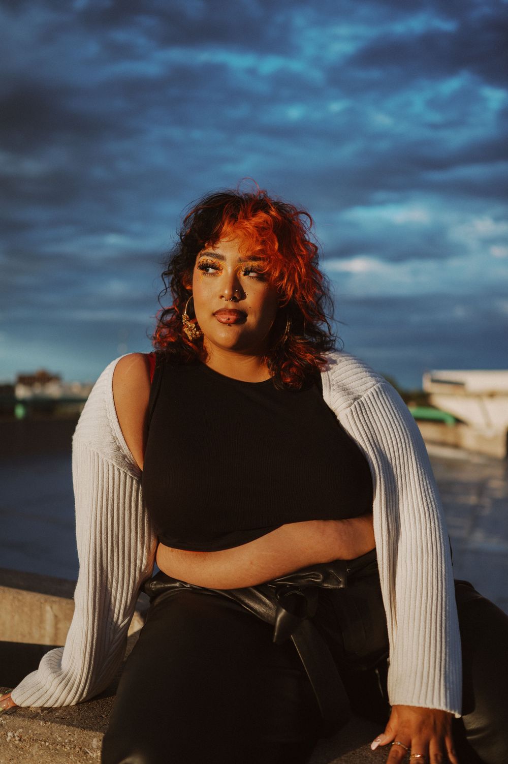 Dramatic portrait photoshoot at sunset featuring a black dress and white sweater against stormy blue clouds.