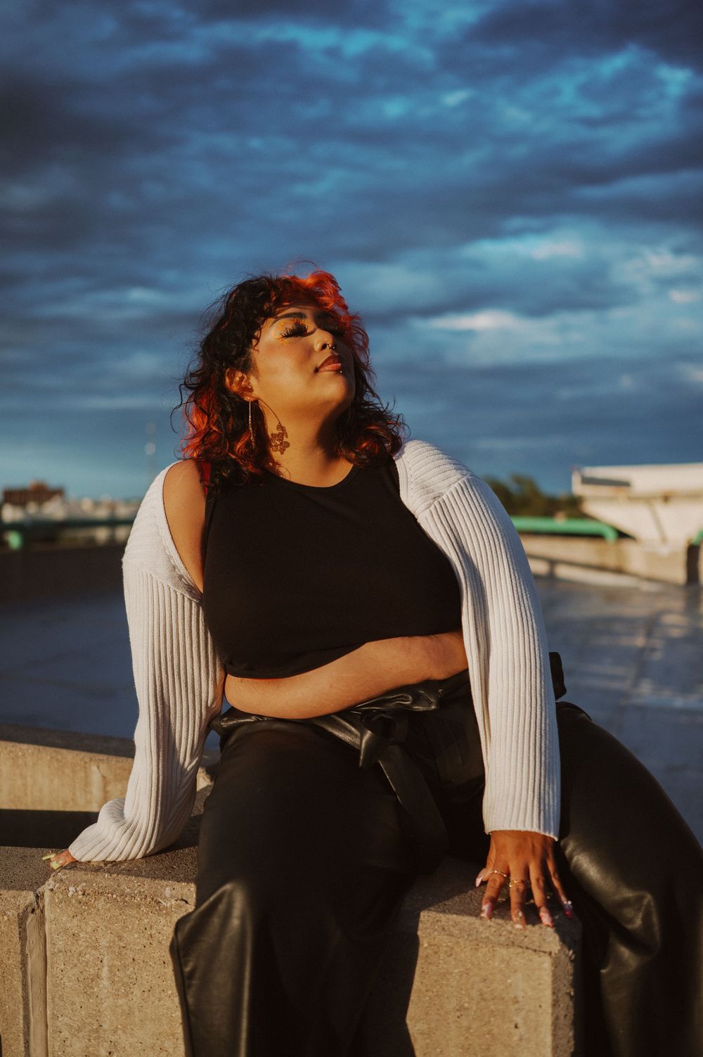 Person in contrasting black and white outfit poses outdoors against dramatic blue cloudy sky at sunset.