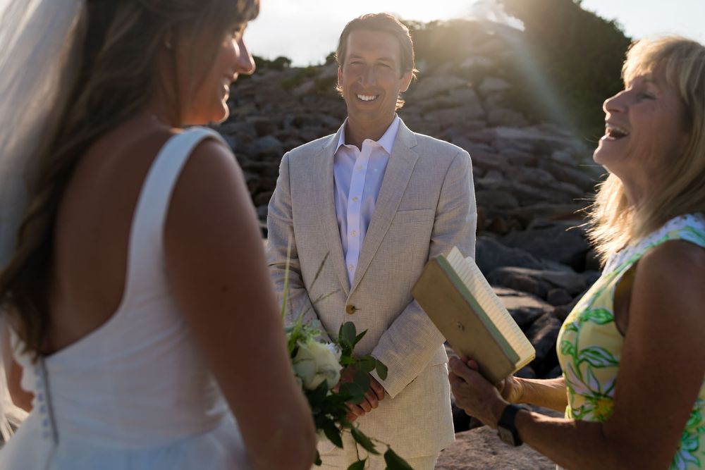 A beaming bride and groom share an intimate moment during their beach wedding ceremony at sunset.