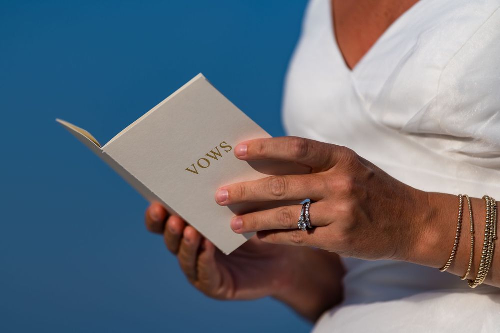 Hand holds a white box labeled Vows against a blue background as part of a wedding ceremony preparation.