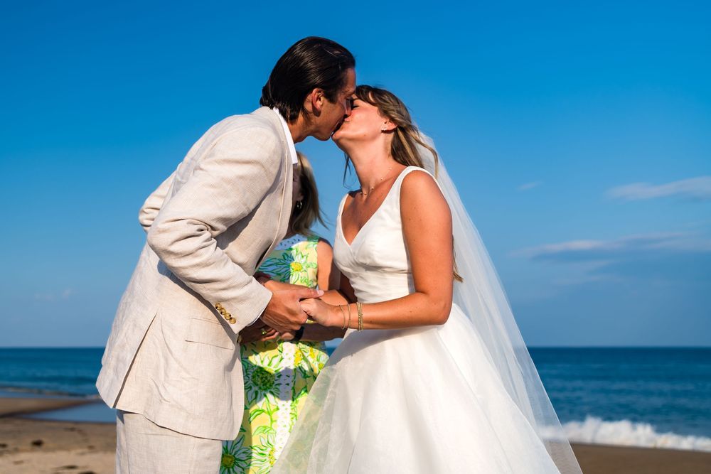 A romantic beachside wedding photoshoot with blue skies and ocean waves in the background.
