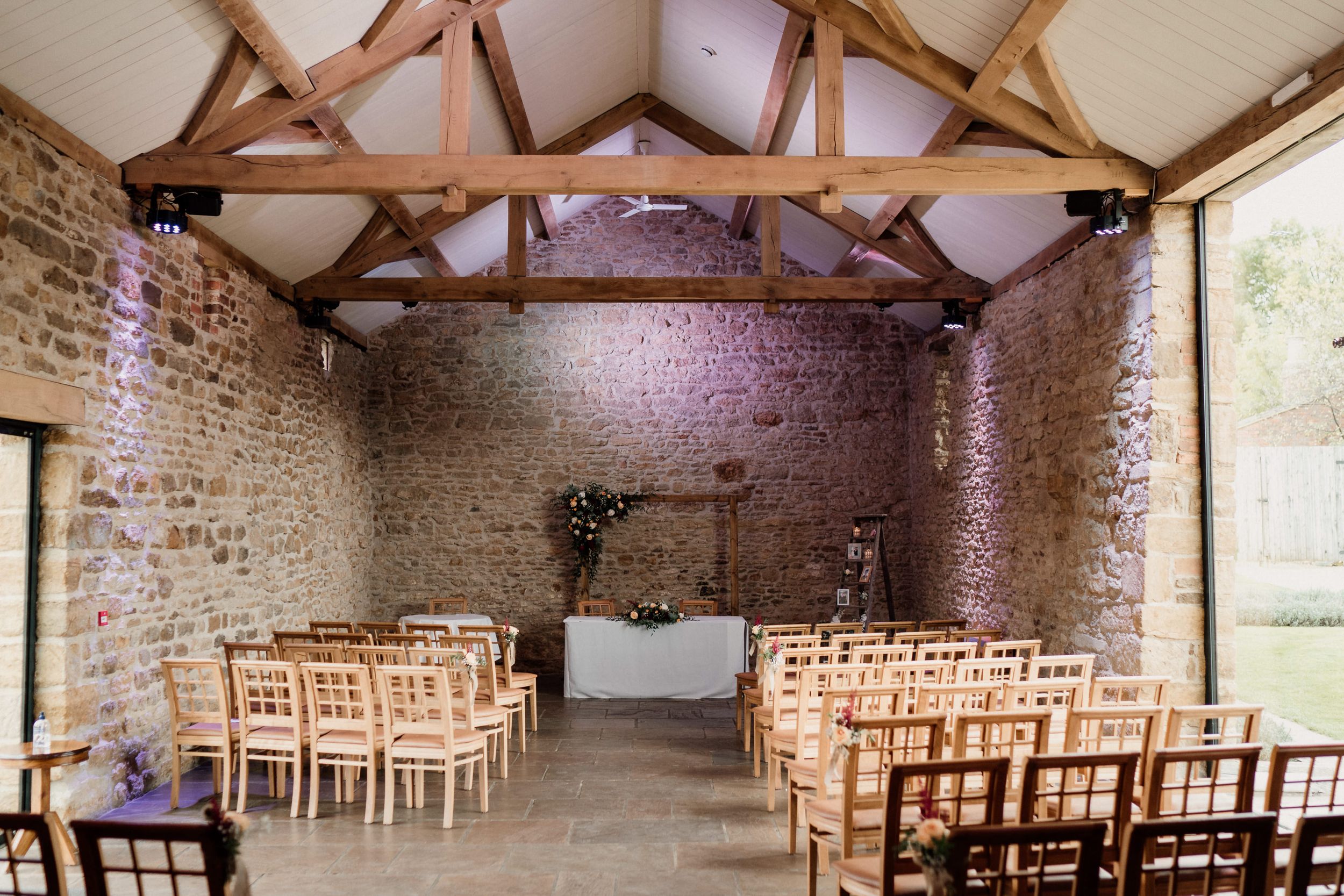 Dodford Manor Rustic barn venue with exposed wooden beams and stone walls set up for wedding ceremony.