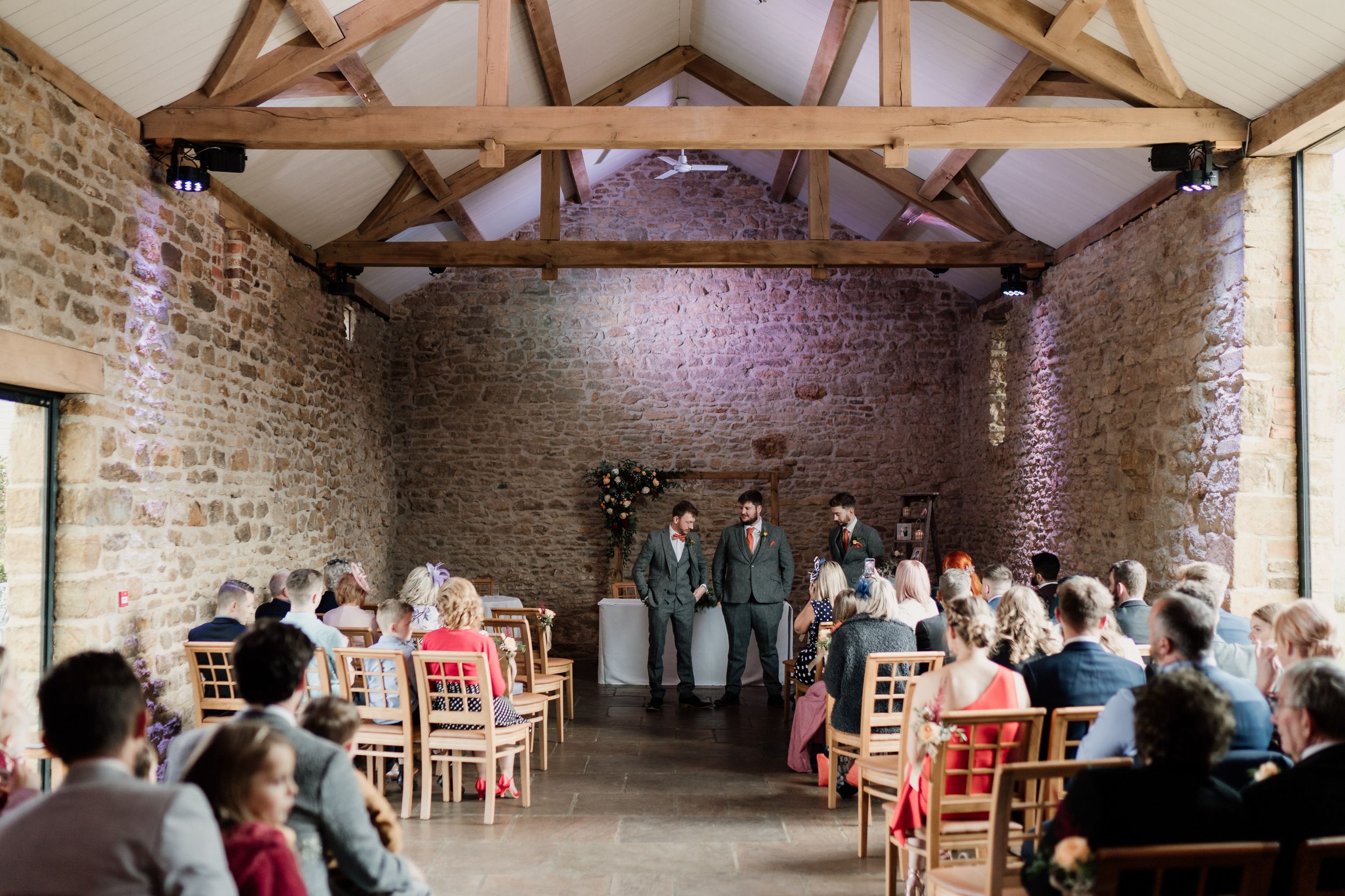 Wedding ceremony setup in a rustic barn venue at Dodford Manor with exposed beams and stone walls.