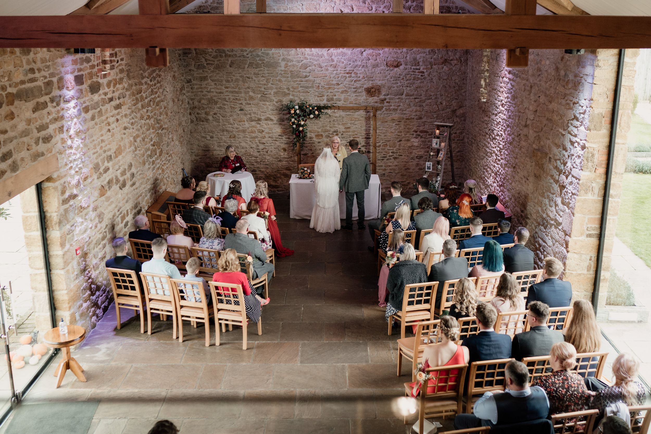 Aerial view of wedding ceremony at Dodford Manor in a converted stone barn with wooden chairs and tables.