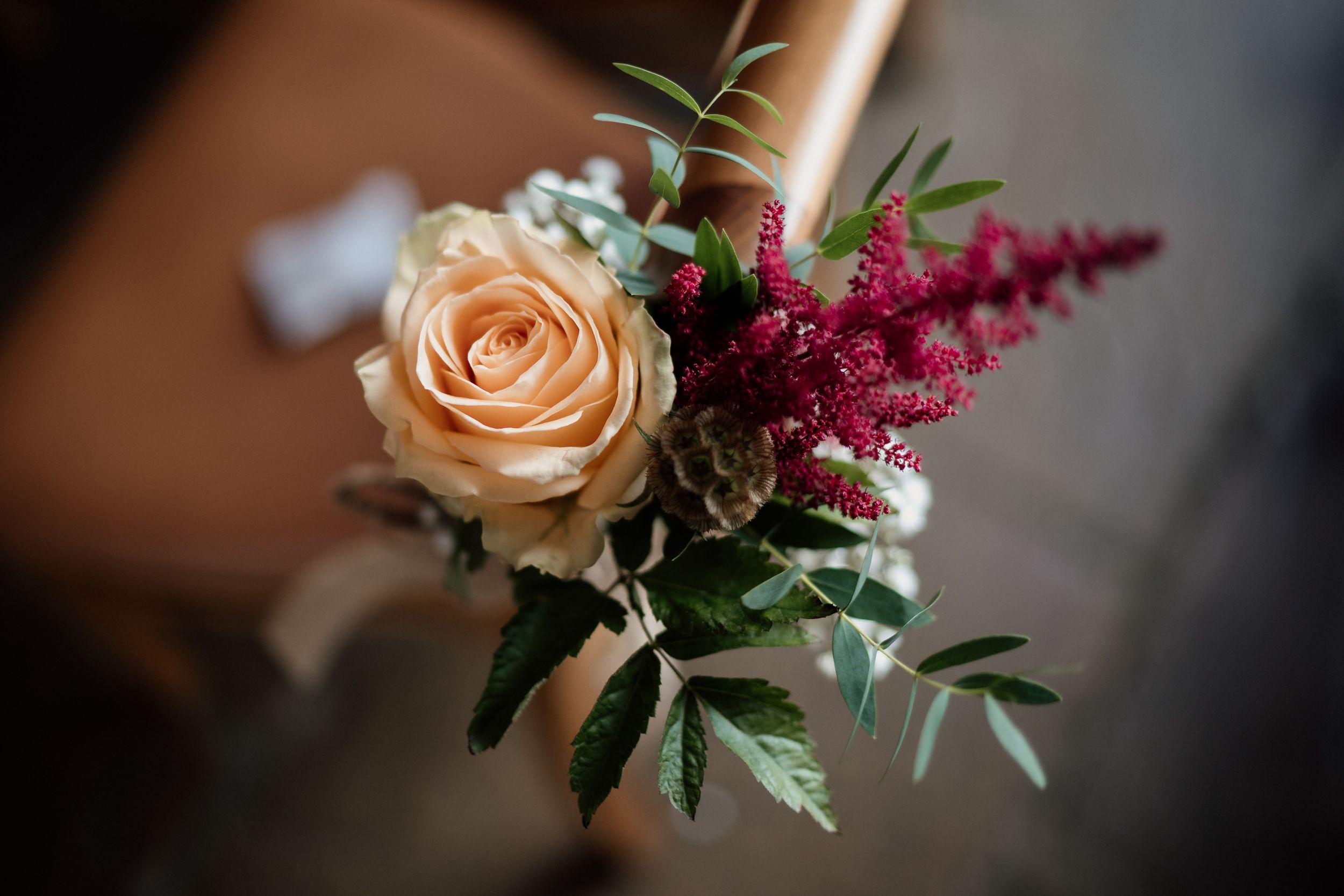 Close-up of a delicate floral arrangement featuring a peach rose and burgundy astilbe with greenery.