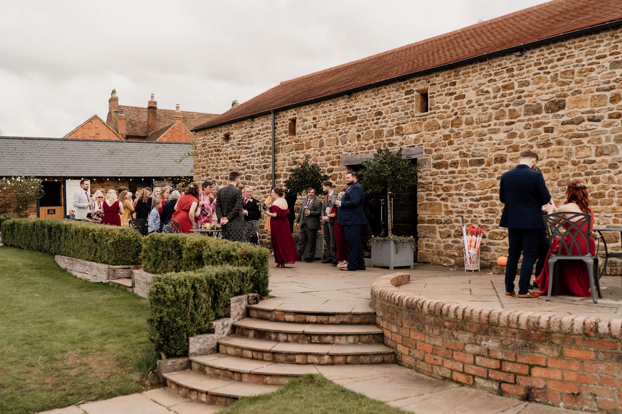 Wedding guests gathering on stone steps outside Dodford Manor Barn.