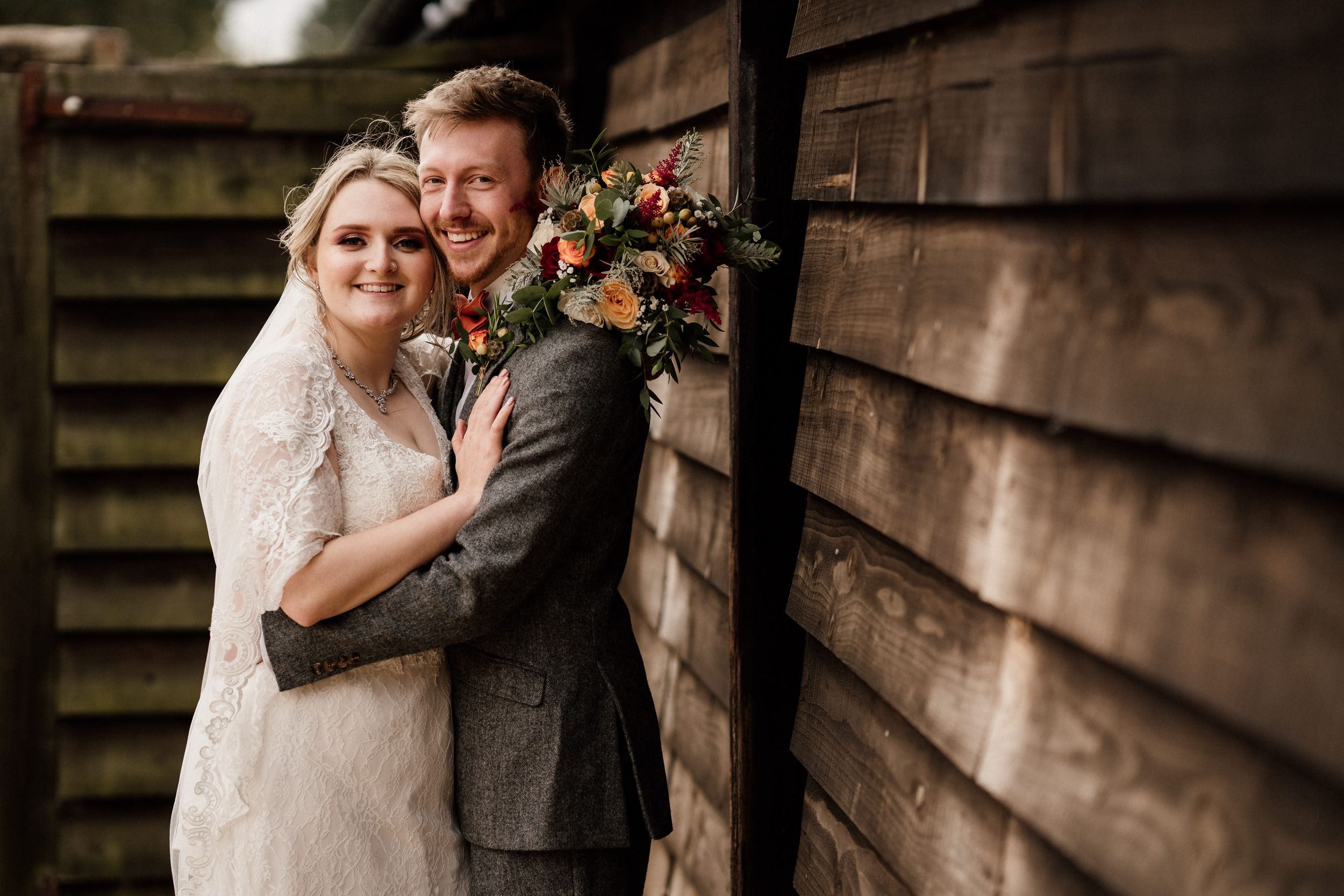 Rustic wedding portrait against wooden barn wall with autumn-colored bouquet.