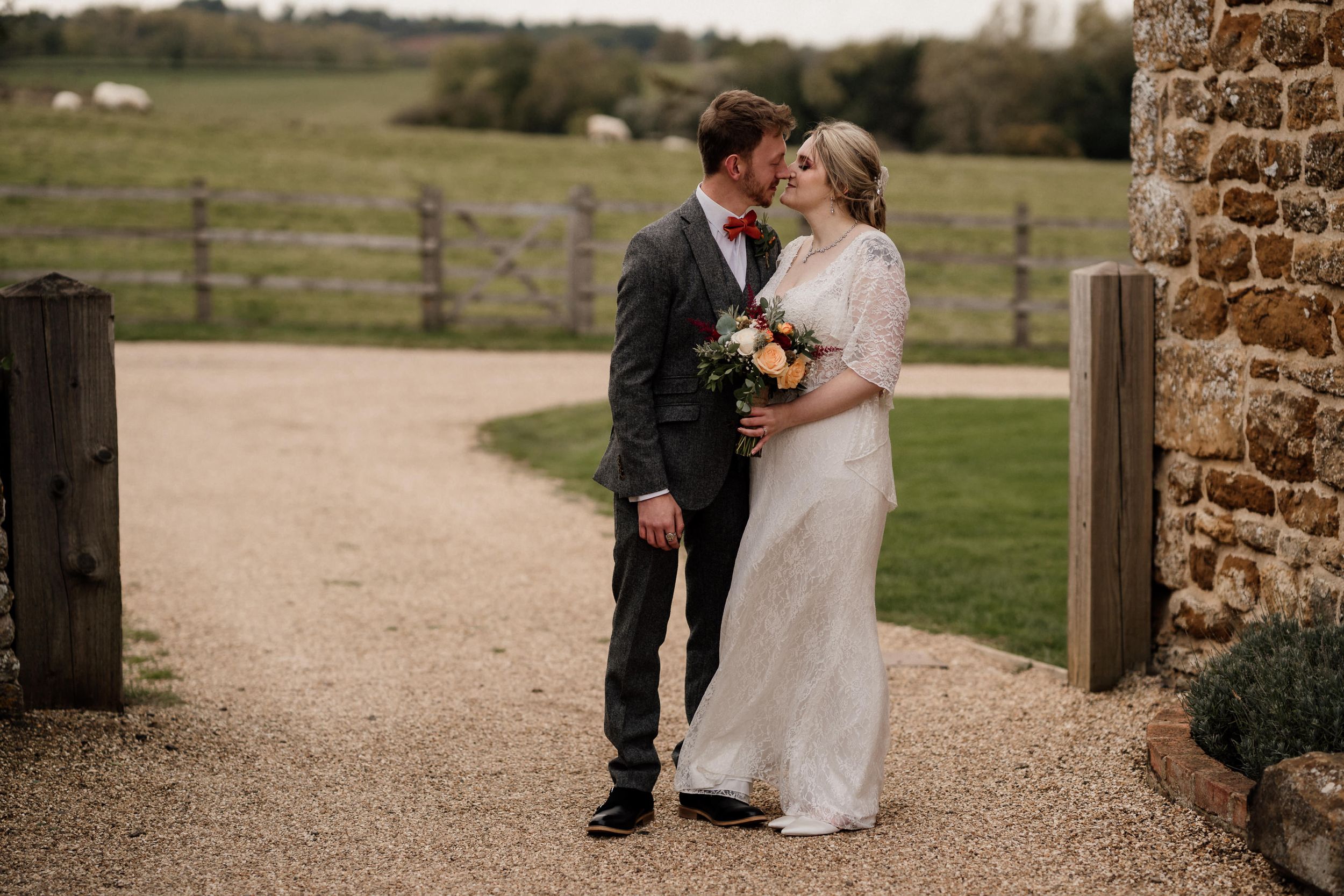 Romantic wedding moment on a countryside path near stone architecture at Dodford Manor Barns.