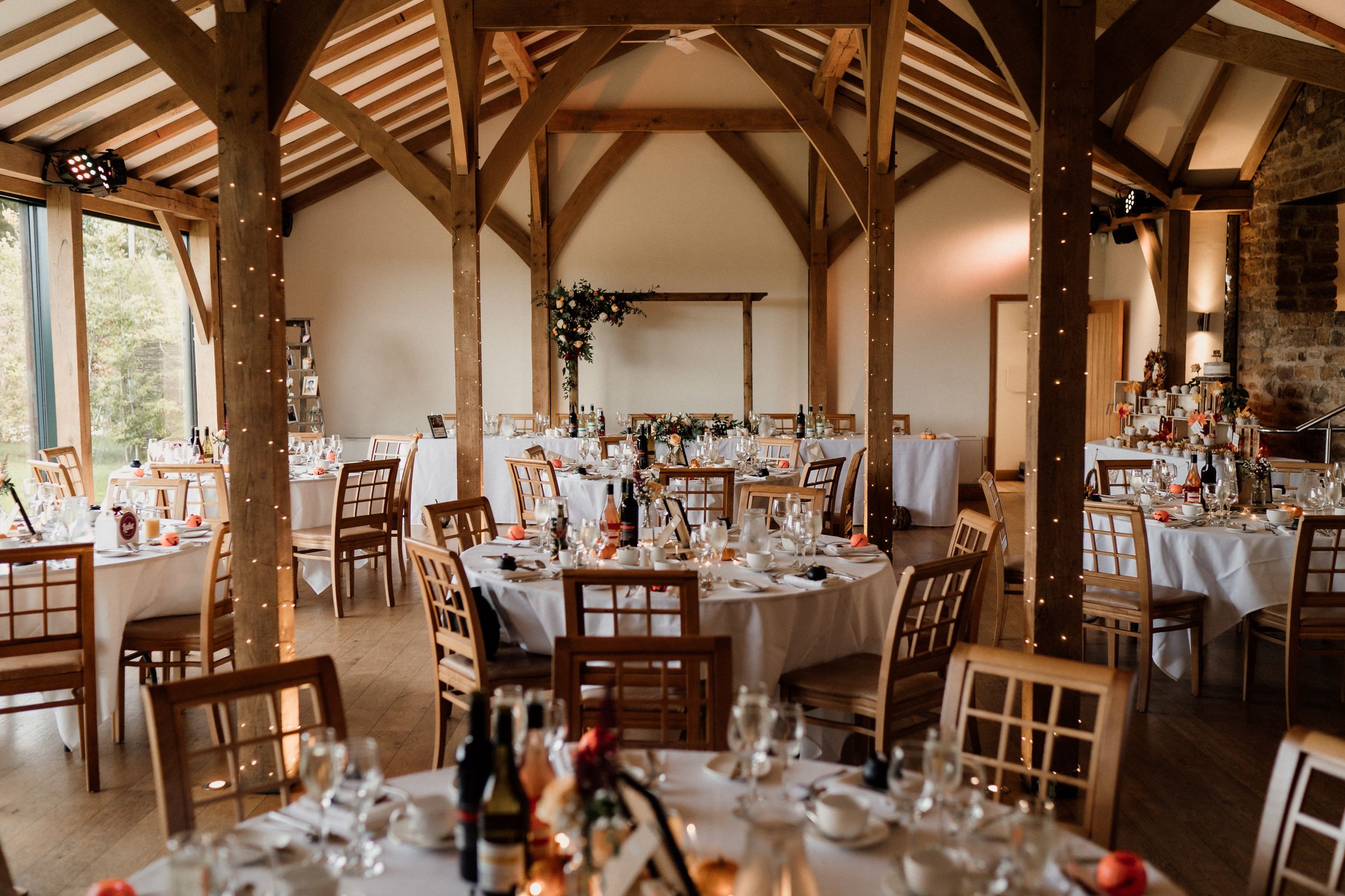Elegant rustic wedding reception venue at Dodford Manor Barns with wooden beams and decorated round tables.