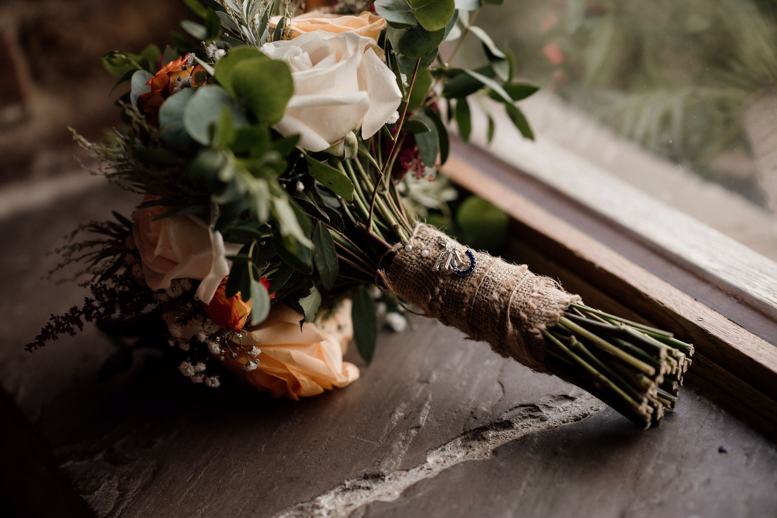Elegant bridal bouquet with roses and greenery wrapped in twine on stone surface.