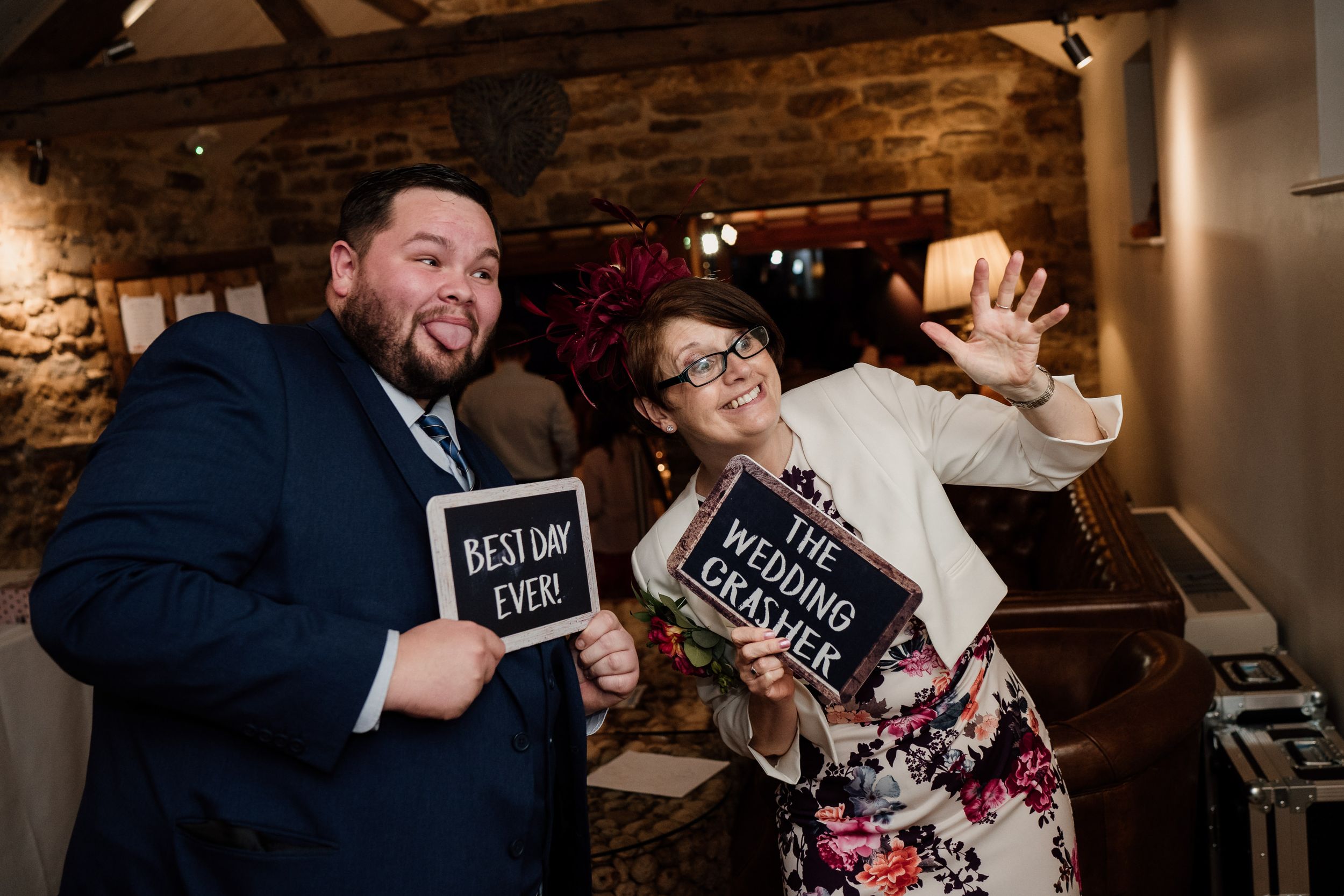 Wedding guests pose with fun photo props at rustic indoor reception venue.